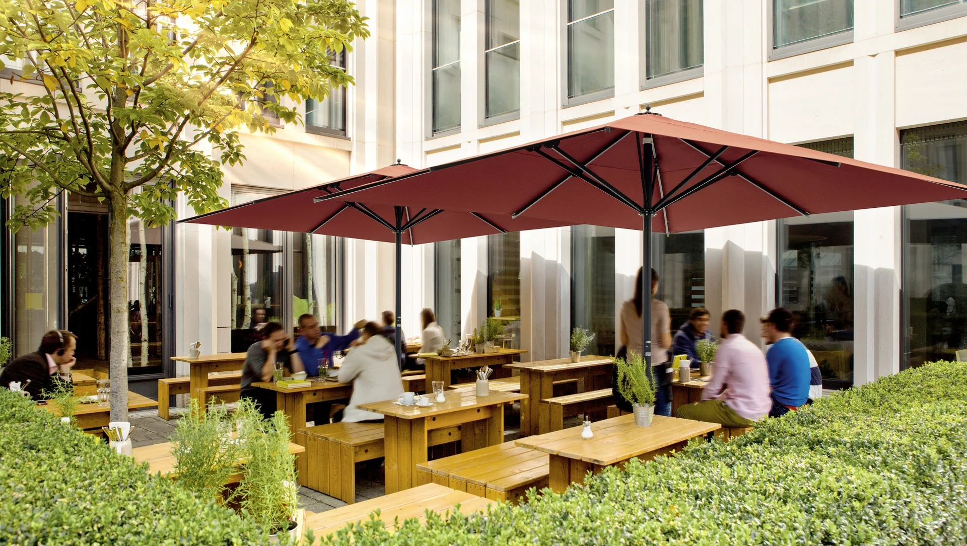Außenbereich eines Cafés mit Holzbänken und rotem Sonnenschirm